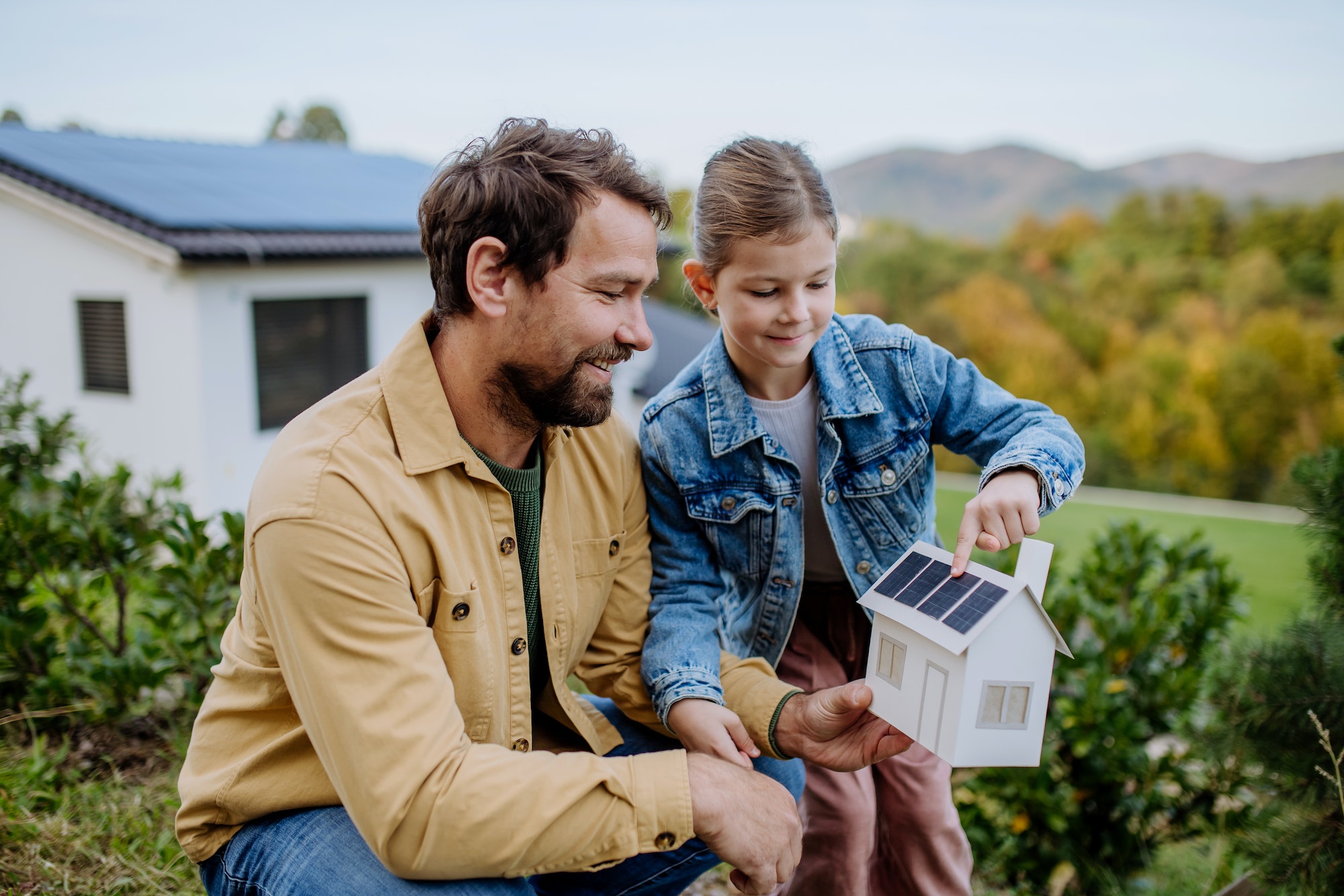 Little girl with her dad holding paper model of house with solar panels, explaining how it works